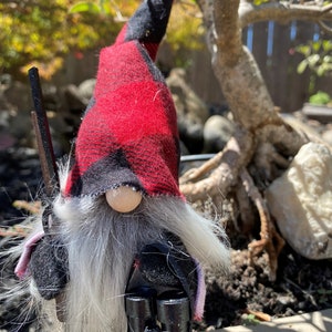May include: A gnome with a long white beard and a red and black checked hat. The gnome is holding a pair of black binoculars and a wooden stick. The gnome is standing in front of a bonsai tree and rocks. The text "4. Hunter" is visible in the image.