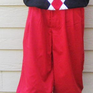 May include: A golf outfit on a mannequin. The outfit includes a black V-neck sweater vest with a red and white argyle pattern, red knickerbockers, argyle socks, and white golf shoes with brown and gold accents.