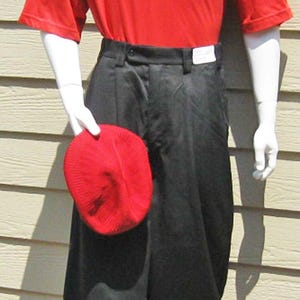 Puede incluir: Maniquí con camisa de golf roja con cuello de rombos blancos y negros, pantalones cortos negros, calcetines de rombos y zapatos de golf bicolor. Se sostiene un gorro de punto rojo en la mano.