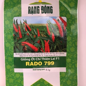 May include: A packet of chili pepper seeds called "RADO 799" with a green background and a picture of red chili peppers. The packet is labeled "Giống Ớt Chỉ Thiên Lai F1" and "Theo TCCS 15:2017/RDHCM". The packet also states "Khối lượng tịnh: 0.1g".