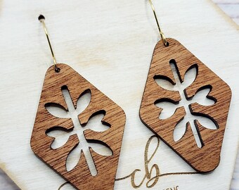 May include: A pair of wooden earrings with a geometric diamond shape and a cutout floral design. The earrings are brown and have gold hooks.