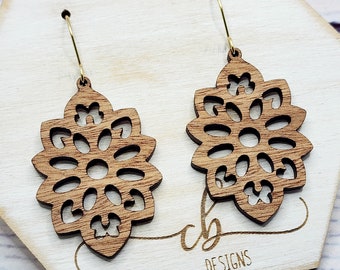 May include: A pair of wooden earrings with a delicate, intricate design. The earrings are brown and have a gold-colored hook.