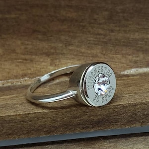 May include: A silver ring with a clear rhinestone set in a silver bullet casing. The bullet casing is engraved with "WINCHESTER 38 SPL."