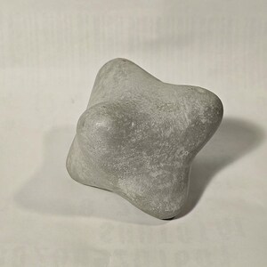 Pode incluir: Um objeto de pedra cinzento, texturizado, de forma irregular com bordas arredondadas.