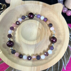 May include: A purple, pink, and white beaded bracelet with silver accents and two dark purple pearl-like beads.