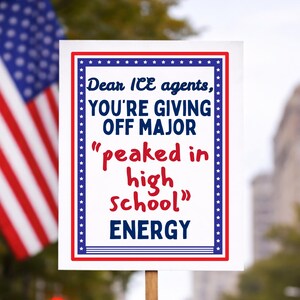 May include: A white sign with a red, white, and blue border and text that reads "Dear ICE agents, YOU'RE GIVING OFF MAJOR 'peaked in high school' ENERGY." An American flag is visible in the background.