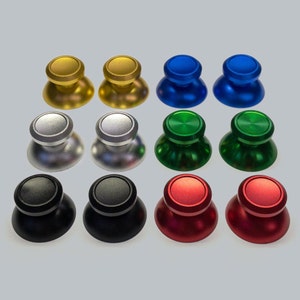 May include: Set of ten different coloured thumbsticks for a gaming controller. The thumbsticks are made of metal and come in gold, silver, blue, green, black, and red.