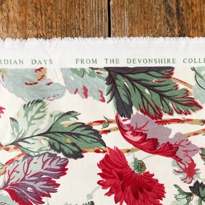 May include: A white fabric with a floral pattern featuring green, red, and purple leaves. The fabric has a label that reads "Edwardian Days from the Devonshire Collection."
