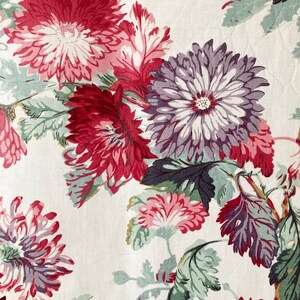 May include: A white fabric with a floral pattern featuring red, pink, and purple flowers with green leaves.