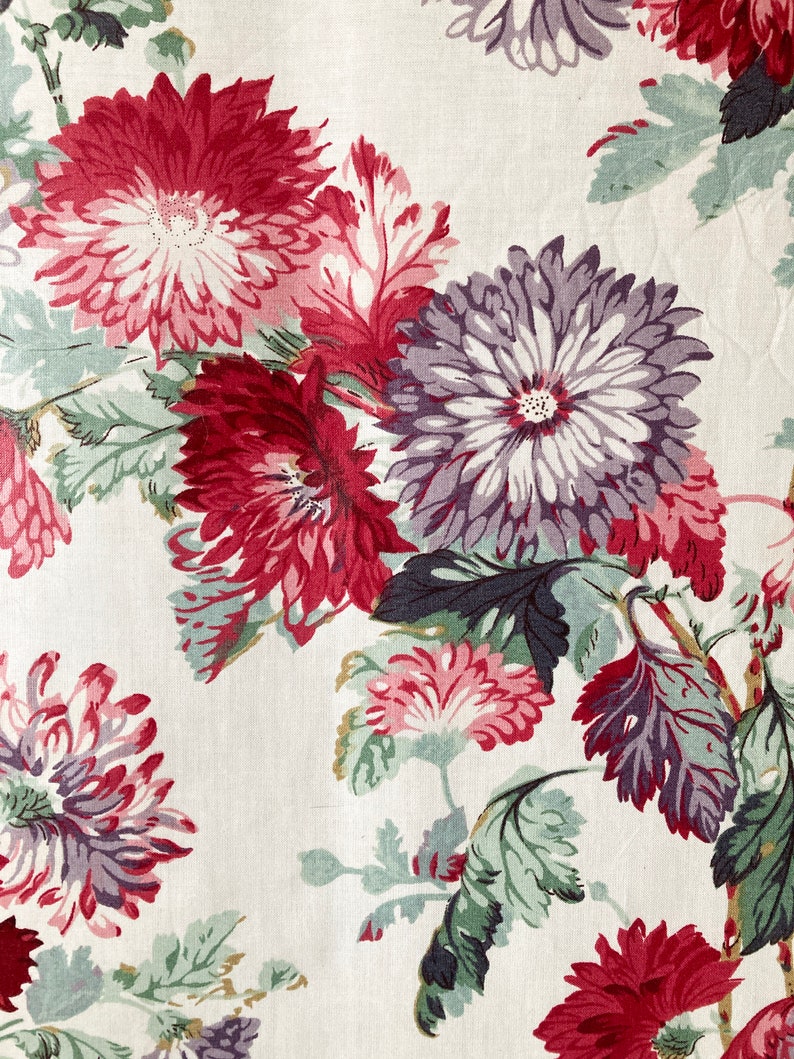 May include: A white fabric with a floral pattern featuring red, pink, and purple flowers with green leaves.