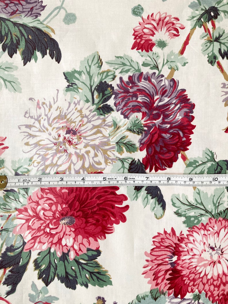 May include: White fabric with a floral print featuring pink, red, and purple flowers. The flowers are stylised and have a vintage look. The fabric is a cotton blend and is perfect for quilting, crafts, and home decor.
