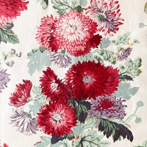 May include: A white fabric with a floral pattern featuring red, pink, and purple flowers with green leaves.