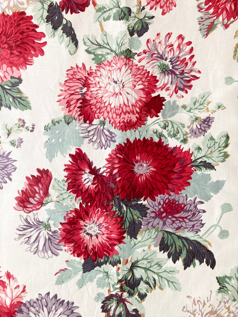May include: A white fabric with a floral pattern featuring red, pink, and purple flowers with green leaves.