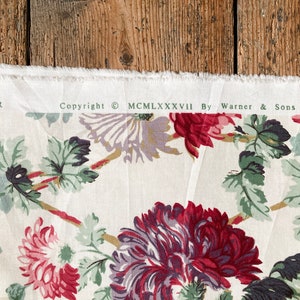 May include: White fabric with a floral print featuring red, purple, and green flowers. The fabric has a copyright notice that reads "Copyright &copy; MCMLXXXVII By Warner & Sons Limited".