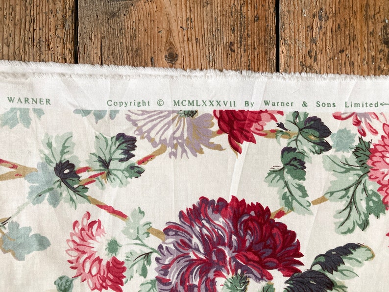 May include: White fabric with a floral print featuring red, purple, and green flowers. The fabric has a copyright notice that reads "Copyright &copy; MCMLXXXVII By Warner & Sons Limited".