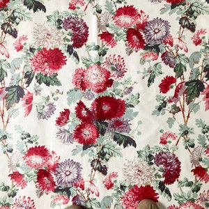 May include: White fabric with a repeating pattern of red, pink, and purple flowers. The flowers are stylised and have a vintage look.