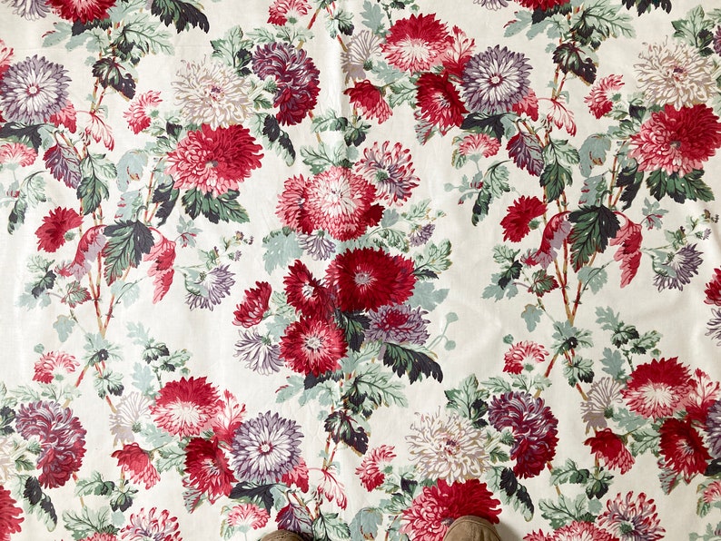 May include: White fabric with a repeating pattern of red, pink, and purple flowers. The flowers are stylised and have a vintage look.