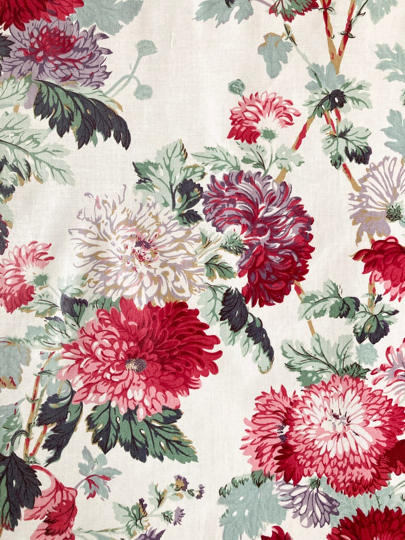 May include: A white fabric with a floral pattern featuring pink, red, and purple flowers with green leaves.