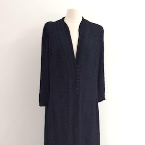 Könnte beinhalten: Ein langes, dunkelmarineblaues Kleid mit V-Ausschnitt und langen Ärmeln. Das Kleid hat Knöpfe auf der Vorderseite und wird auf einer Holzpuppe präsentiert. Das bodenlange Kleid hat ein strukturiertes Muster. Ca. 150 cm lang.