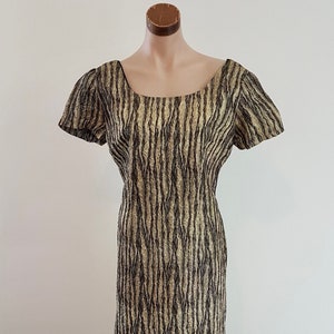 May include: A vintage dress with a black and gold abstract pattern. The dress has a scoop neck and short sleeves. It is made of a textured fabric.