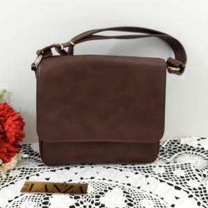 May include: A brown leather shoulder bag with a flap closure and a gold metal logo that says "LANZA".