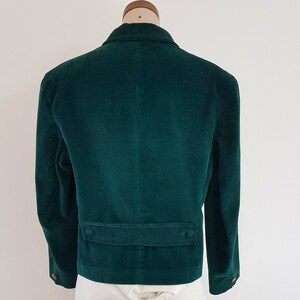 K&ouml;nnte beinhalten: Ein dunkelgr&uuml;ner Cordblazer mit einem einzigen Knopfverschluss und zwei Taschen auf der Vorderseite. Der Blazer hat eine klassische Passform und ist aus einem weichen, bequemen Stoff gefertigt.