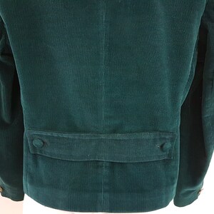 K&ouml;nnte beinhalten: Eine dunkelgr&uuml;ne Cordjacke mit einer Patte auf der R&uuml;ckseite. Die Jacke hat zwei Kn&ouml;pfe auf der Patte.