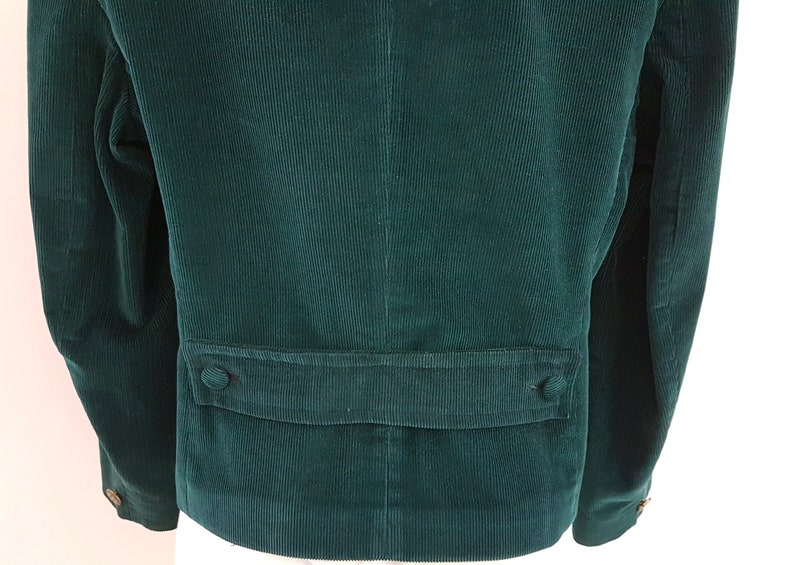 K&ouml;nnte beinhalten: Eine dunkelgr&uuml;ne Cordjacke mit einer Patte auf der R&uuml;ckseite. Die Jacke hat zwei Kn&ouml;pfe auf der Patte.
