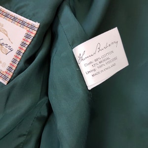K&ouml;nnte beinhalten: Wei&szlig;es Etikett mit schwarzem Text, der "Thomas Burberry" lautet und die Stoffzusammensetzung detailliert: "Cloth: 88% Baumwolle 12% Modal" und "Lining: 100% Viskose". Das Etikett tr&auml;gt au&szlig;erdem den Hinweis "Made in England".