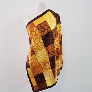 May include: A yellow and brown patterned silk scarf with a geometric design. The scarf is folded and draped over a white mannequin.