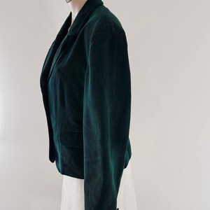 K&ouml;nnte beinhalten: Ein dunkelgr&uuml;ner Cordblazer mit klassischem Kragen und langen &Auml;rmeln. Der Blazer hat einen einzigen Knopfverschluss und zwei Taschen.