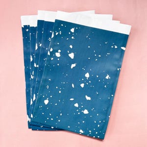 Op de afbeelding: Een stapel van zes blauwe cadeauzakken met een wit gespikkeld patroon. De zakken zijn gemaakt van papier en hebben een witte rand aan de bovenkant.