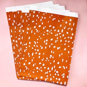 Op de afbeelding: Een stapel van vijf oranje stoffen vierkanten met een wit stippenpatroon. De stof heeft een witte rand.