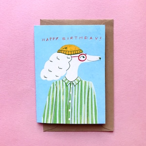 Op de afbeelding: Een kaart met een cartoonillustratie van een witte hond die een gele hoed en een rode bril draagt. De hond draagt een groen-wit gestreept shirt. De kaart zegt "Happy Birthday!" in rode letters.