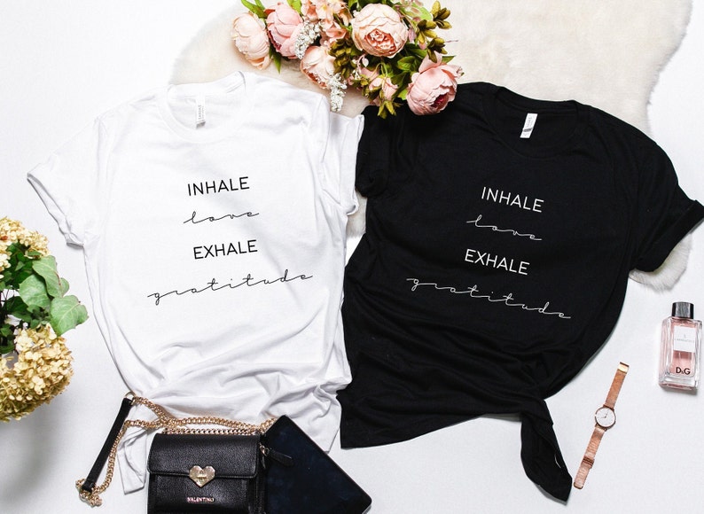 May include: Two t-shirts with the text "INHALE love EXHALE gratitude" printed on them. One t-shirt is white and the other is black.