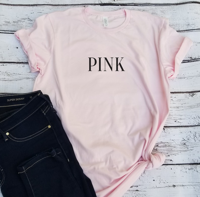 May include: A pink t-shirt with the word "PINK" printed in black on the front.