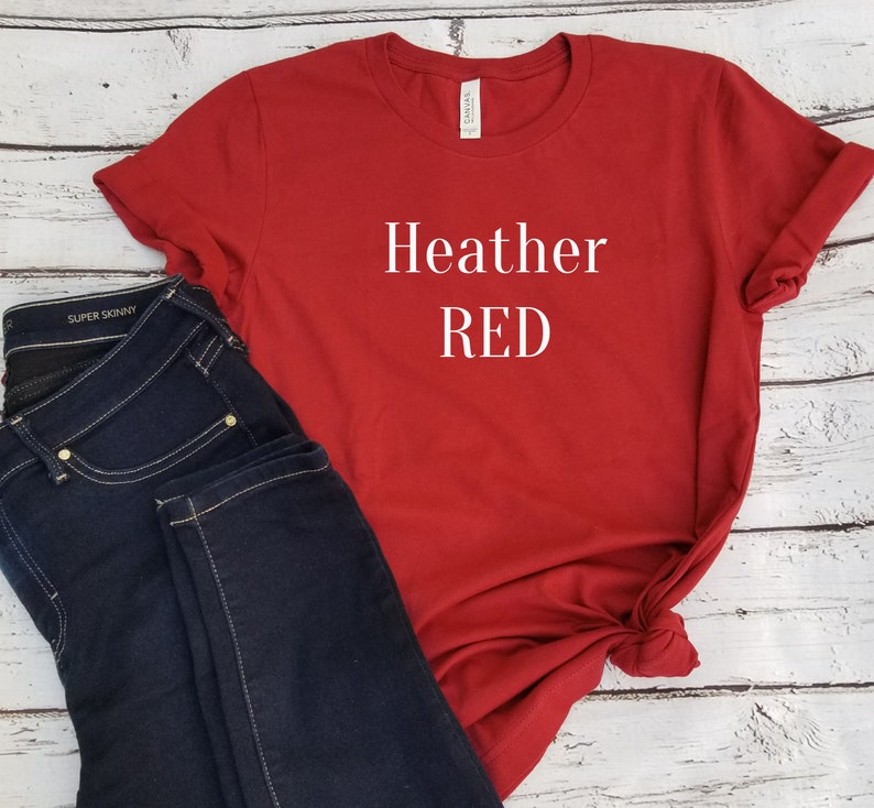 May include: Red t-shirt with the text "Heather RED" printed in white on the front. The shirt is paired with dark blue jeans.