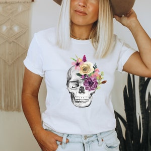May include: White t-shirt with a floral skull graphic. The skull is gray and white with purple, pink, yellow, and white flowers covering one eye.