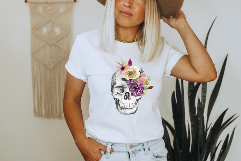 May include: White t-shirt with a floral skull graphic. The skull is gray and white with purple, pink, yellow, and white flowers covering one eye.