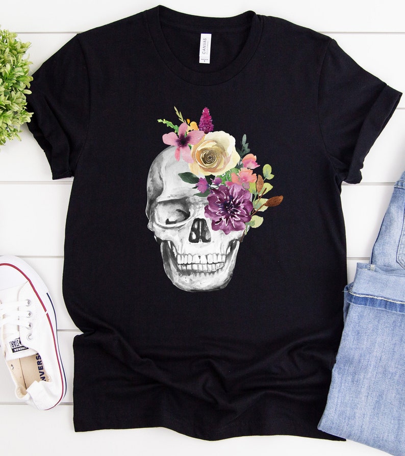 May include: Black t-shirt with a white skull design. The skull's eye socket is filled with a bouquet of purple, pink, and yellow flowers.
