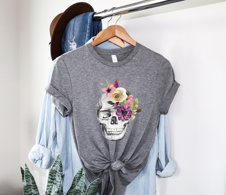 May include: Gray t-shirt with a floral skull design. The skull is white with black eye sockets and a black nose. The flowers are pink, yellow, purple, and green.