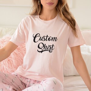 May include: A pink t-shirt with the text "Custom Shirt" in black script font.