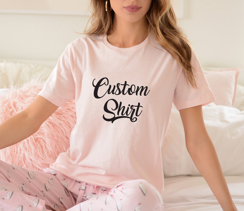 May include: A pink t-shirt with the text "Custom Shirt" in black script font.