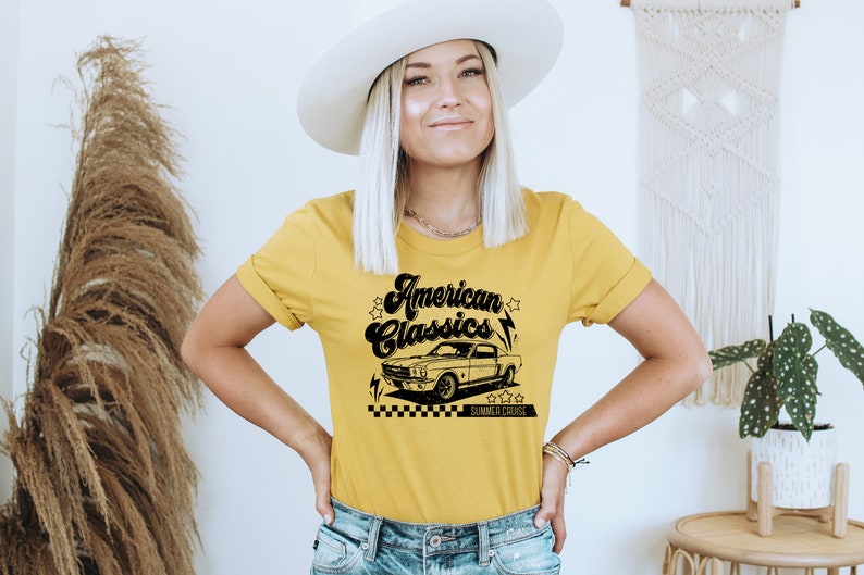 Puede incluir: Una camiseta amarilla con un gr&aacute;fico negro de un coche cl&aacute;sico y el texto "American Classics" en una fuente retro. El gr&aacute;fico tambi&eacute;n incluye estrellas y rayos.