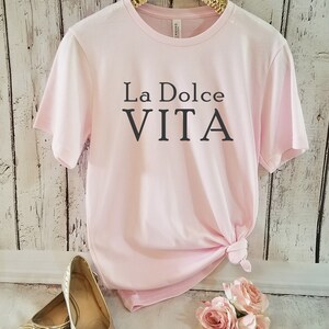May include: A pink t-shirt with the text "La Dolce Vita" printed in black on the front.