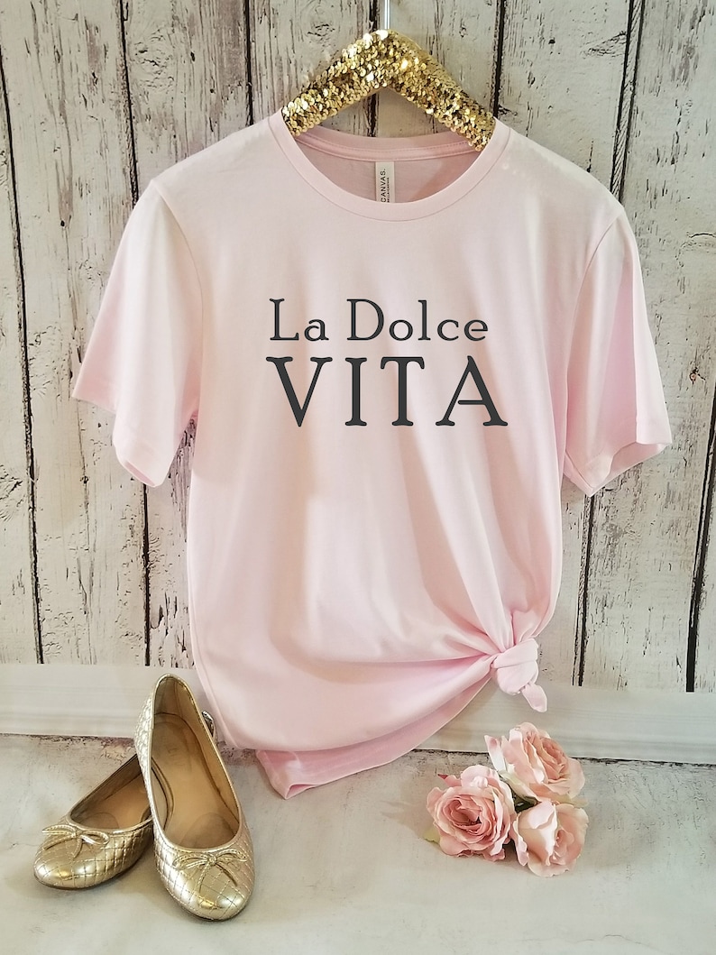 May include: A pink t-shirt with the text "La Dolce Vita" printed in black on the front.