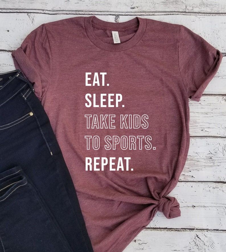 May include: A maroon t-shirt with white text that reads "Eat. Sleep. Take Kids To Sports. Repeat."