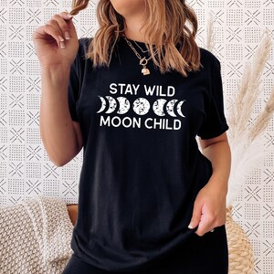 Peut inclure: T-shirt noir avec un texte blanc qui dit "Stay Wild Moon Child" et un graphique d'un croissant de lune dans diff&eacute;rentes phases.