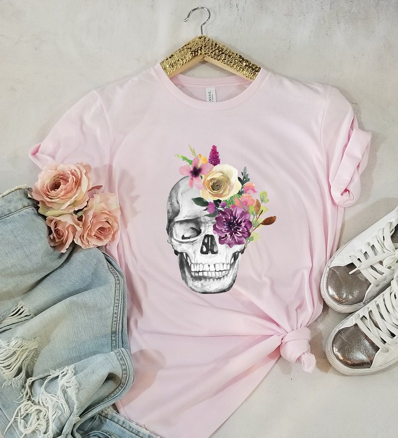 May include: A pink t-shirt with a floral skull graphic. The skull is gray and white with pink, purple, and yellow flowers.