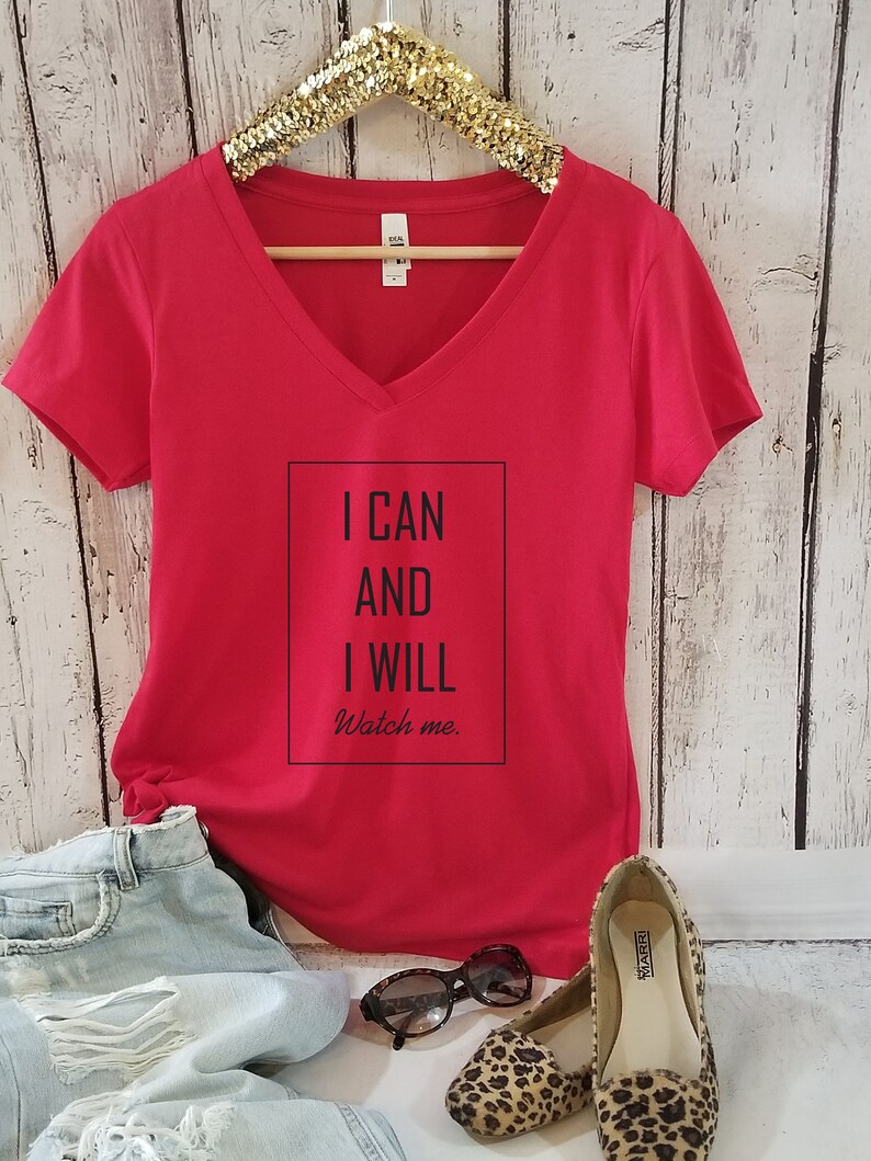 May include: Red v-neck t-shirt with the text "I CAN AND I WILL Watch me." printed on the front.